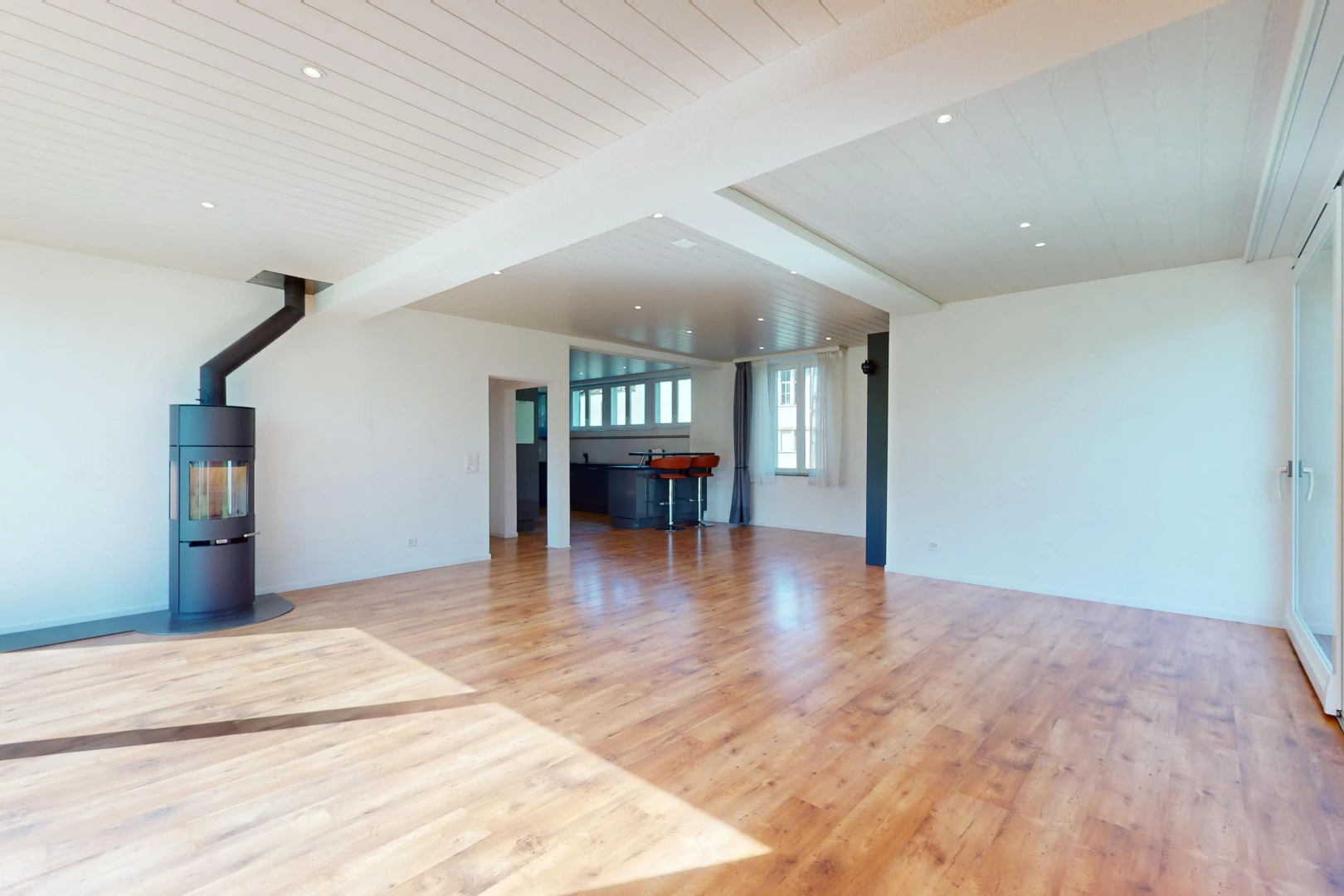 pièce vide avec lumière naturelle, plancher de bois, poutres apparentes, et chaudière