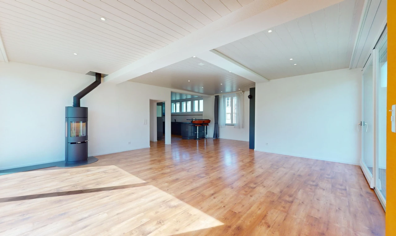 pièce vide avec lumière naturelle, plancher de bois, poutres apparentes, et chaudière