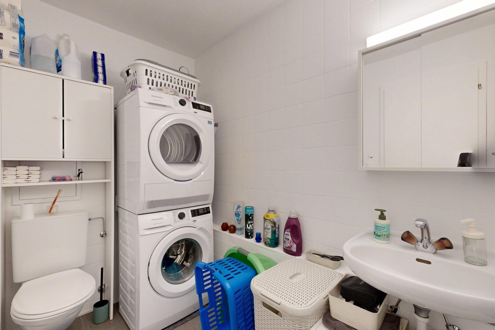 salle de bains avec toilette, inside property, lave-linge et sèche-linge superposés, évier, et miroir