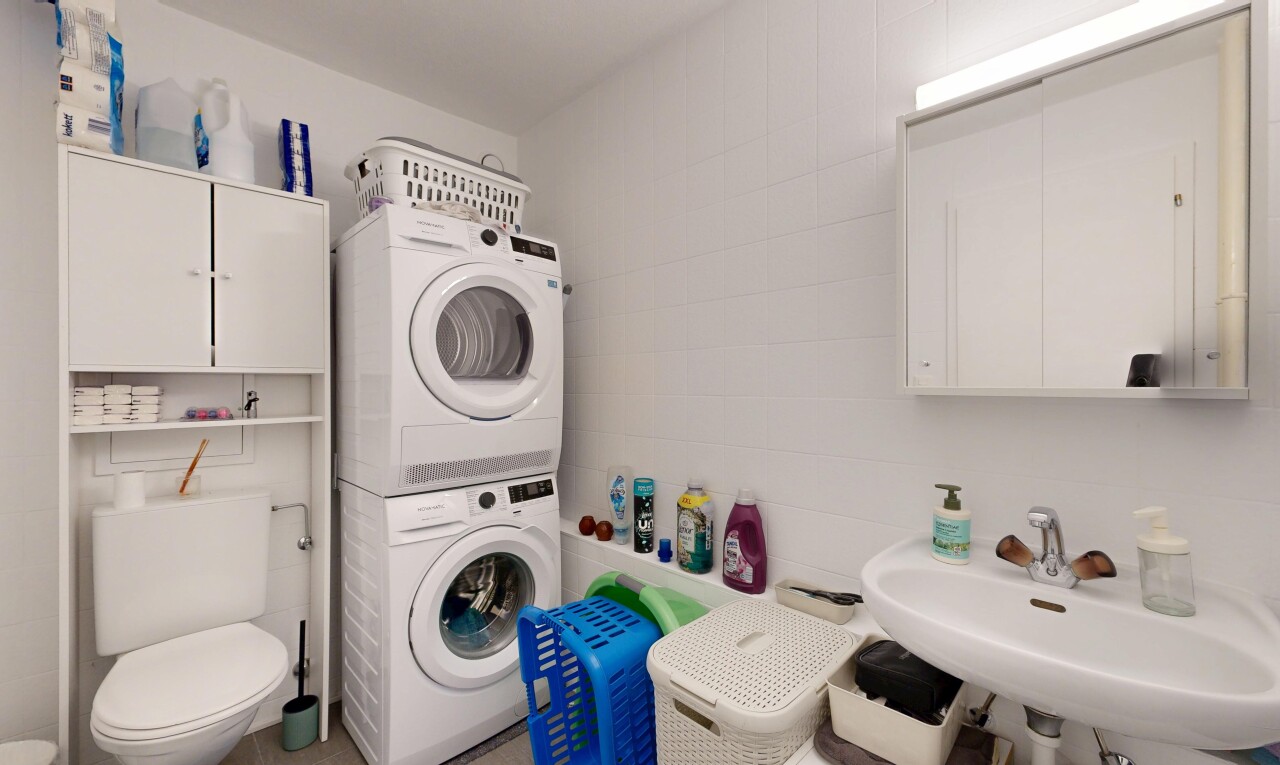 salle de bains avec toilette, inside property, lave-linge et sèche-linge superposés, évier, et miroir