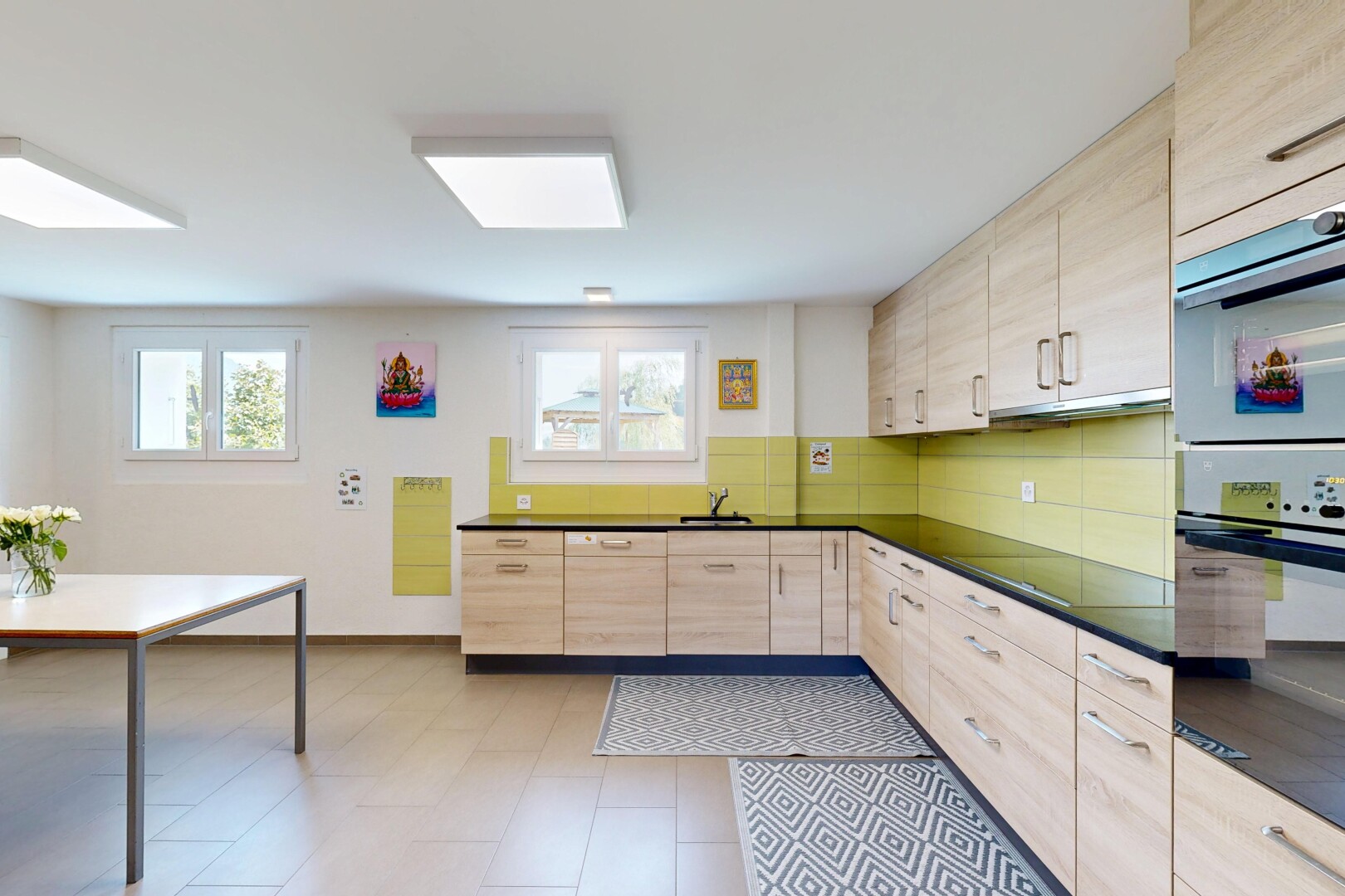 kitchen featuring light wood finish cabinetry, dark countertops, double wall oven, and black electric cooktop