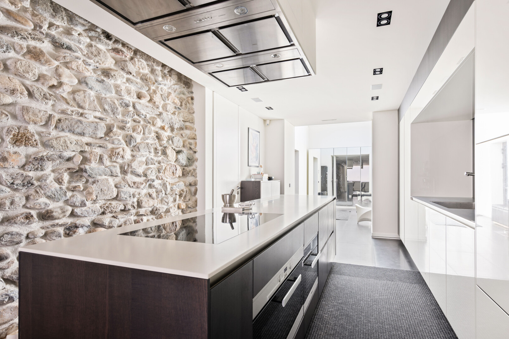 cuisine avec hotte, light countertops, stone wall, armoires à panneau plat, et flat panel cabinets