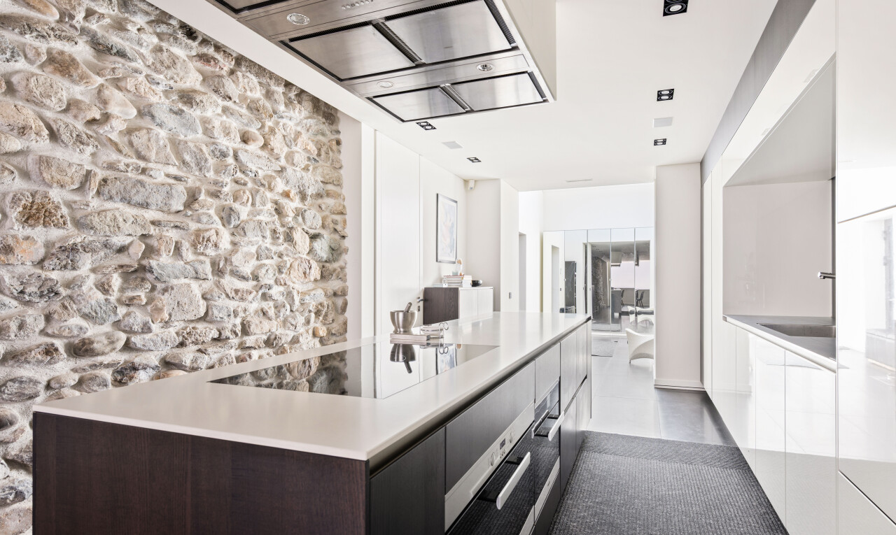 cuisine avec hotte, light countertops, stone wall, armoires à panneau plat, et flat panel cabinets