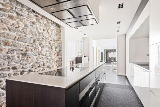 cuisine avec hotte, light countertops, stone wall, armoires à panneau plat, et flat panel cabinets