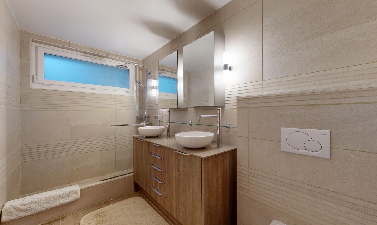 salle de bains avec salle de bain complète, double vasque, miroir, douche, et mur en carrelage