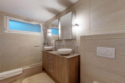 salle de bains avec salle de bain complète, double vasque, miroir, douche, et mur en carrelage