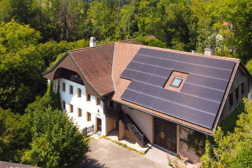 view of property featuring solar panels, a chimney, a view of trees, roof with shingles, and stucco siding