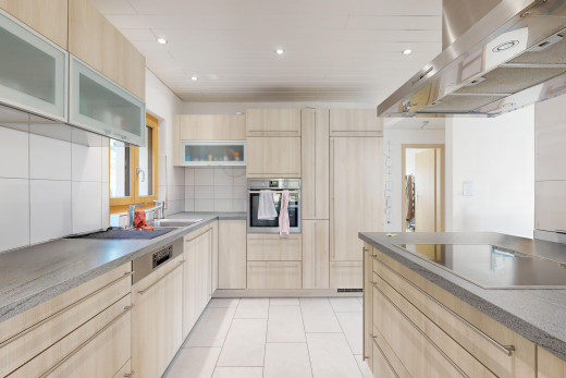 küche mit dunstabzugshaube, hellbraune schränke, schränke mit glastüren, ofen, und fliesenboden