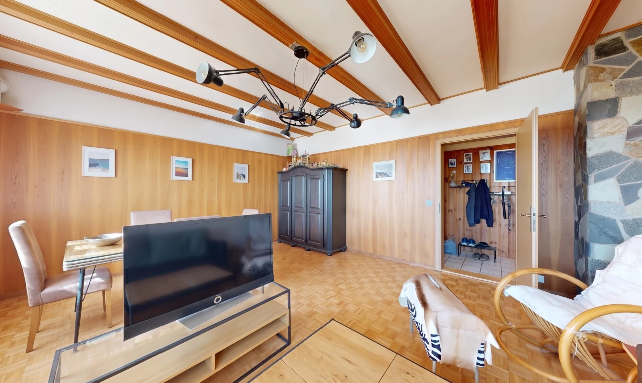 salon avec télévision, plafond à poutres, beamed ceiling, sol en finition bois, et wood finish floor