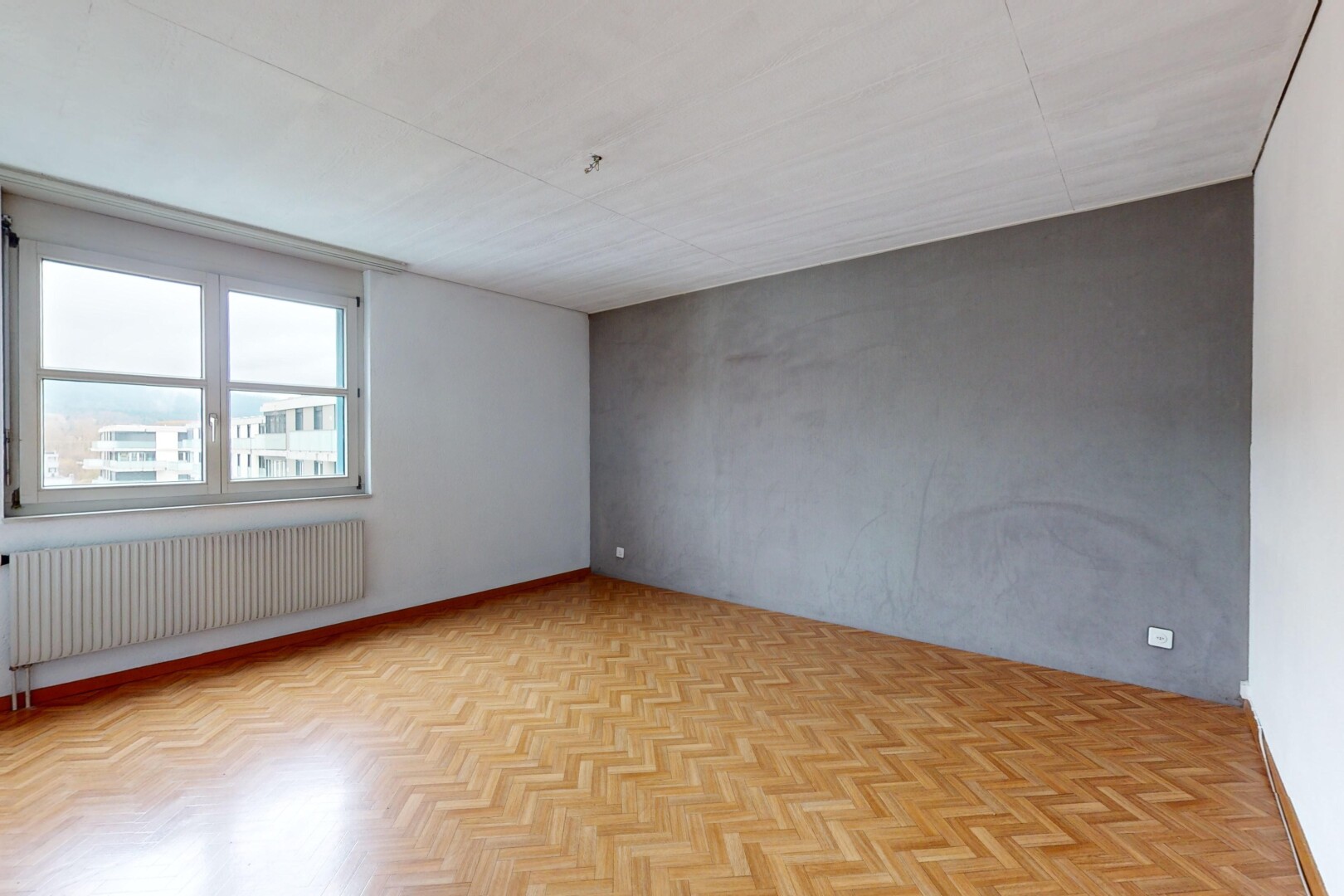 pièce vide avec radiateur, mur en béton, lumière naturelle, et parquet