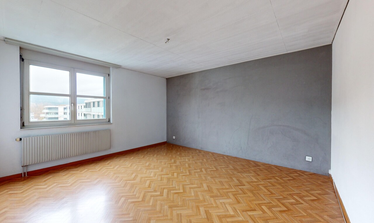 pièce vide avec radiateur, mur en béton, lumière naturelle, et parquet
