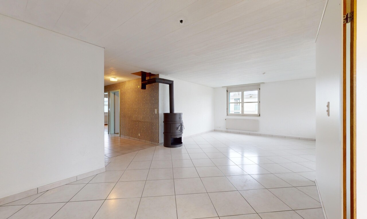pièce vide avec carrelage, lumière naturelle, et poêle à bois