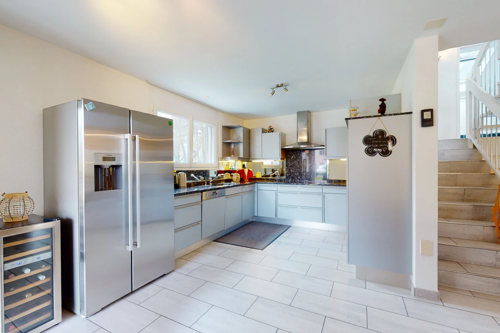 cuisine avec acier inoxydable, carrelage, hotte, réfrigérateur, meubles blancs, plan de travail foncé, et sol clair