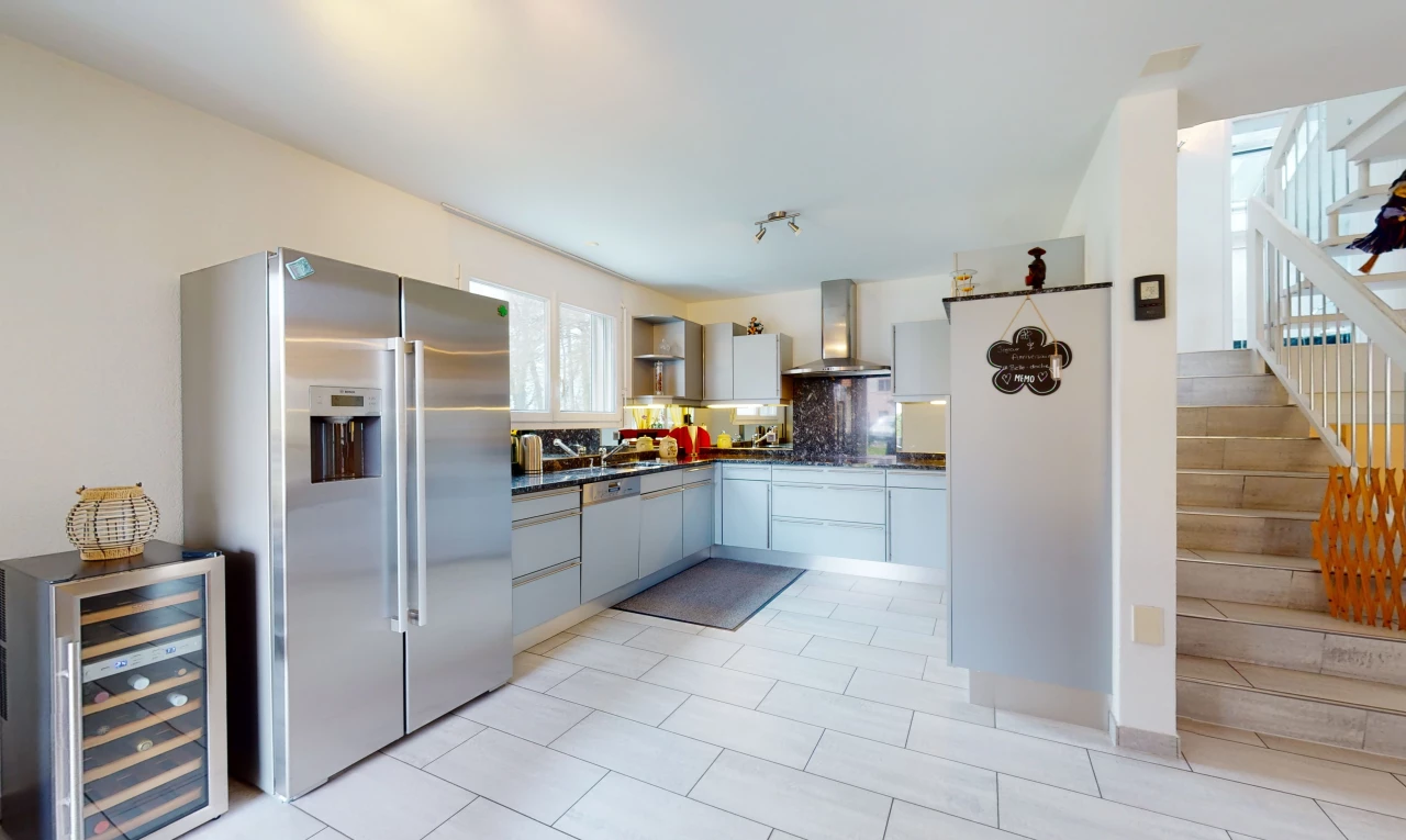 cuisine avec acier inoxydable, carrelage, hotte, réfrigérateur, meubles blancs, plan de travail foncé, et sol clair