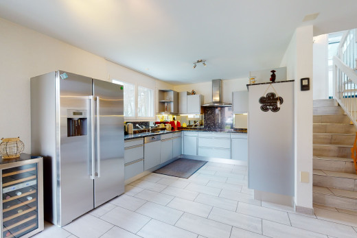 cuisine avec acier inoxydable, carrelage, hotte, réfrigérateur, meubles blancs, plan de travail foncé, et sol clair
