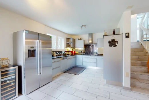 cuisine avec acier inoxydable, carrelage, hotte, réfrigérateur, meubles blancs, plan de travail foncé, et sol clair