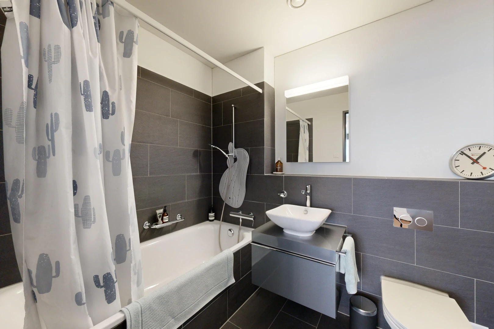 salle de bains avec vasque, toilettes, miroir, mur carrelé, et bain-douche