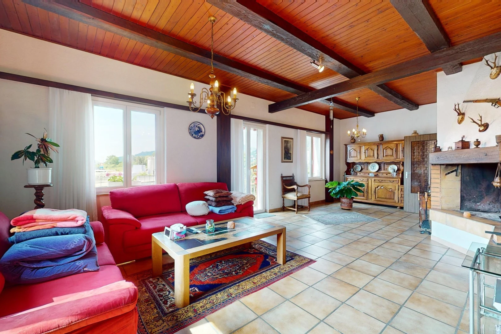 salon avec cheminée, lustre, poutres apparentes, lumière naturelle, et carrelage