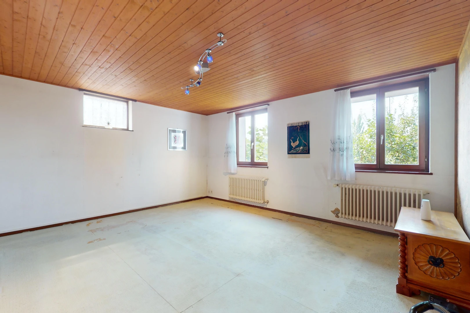 pièce vide avec radiateur, sol en béton, lumière naturelle, et plafond de bois