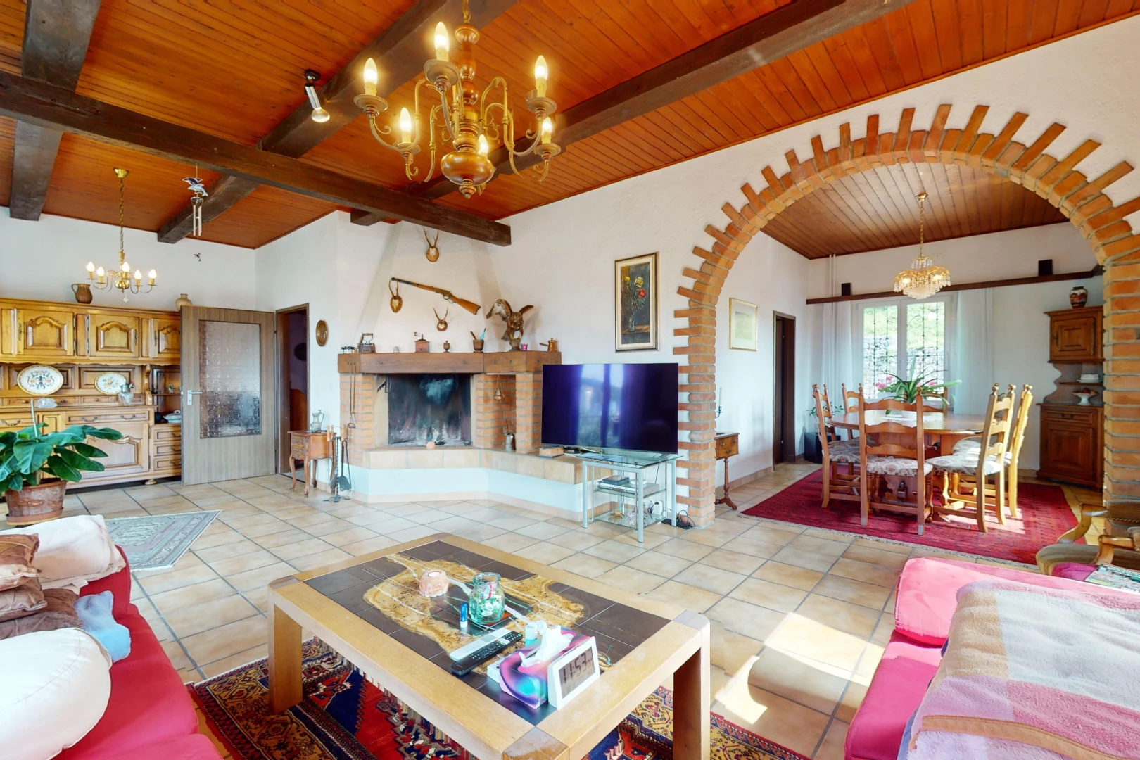 salon / salle à manger avec carrelage, lumière naturelle, télévision, passerelles voûtées, et poutres apparentes