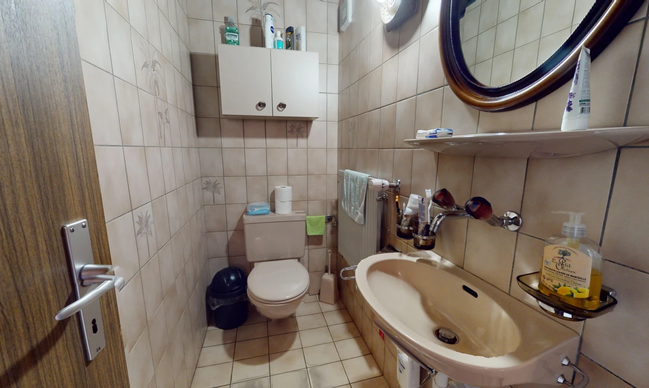 salle de bains avec carrelage, miroir, toilettes, et mur carrelé