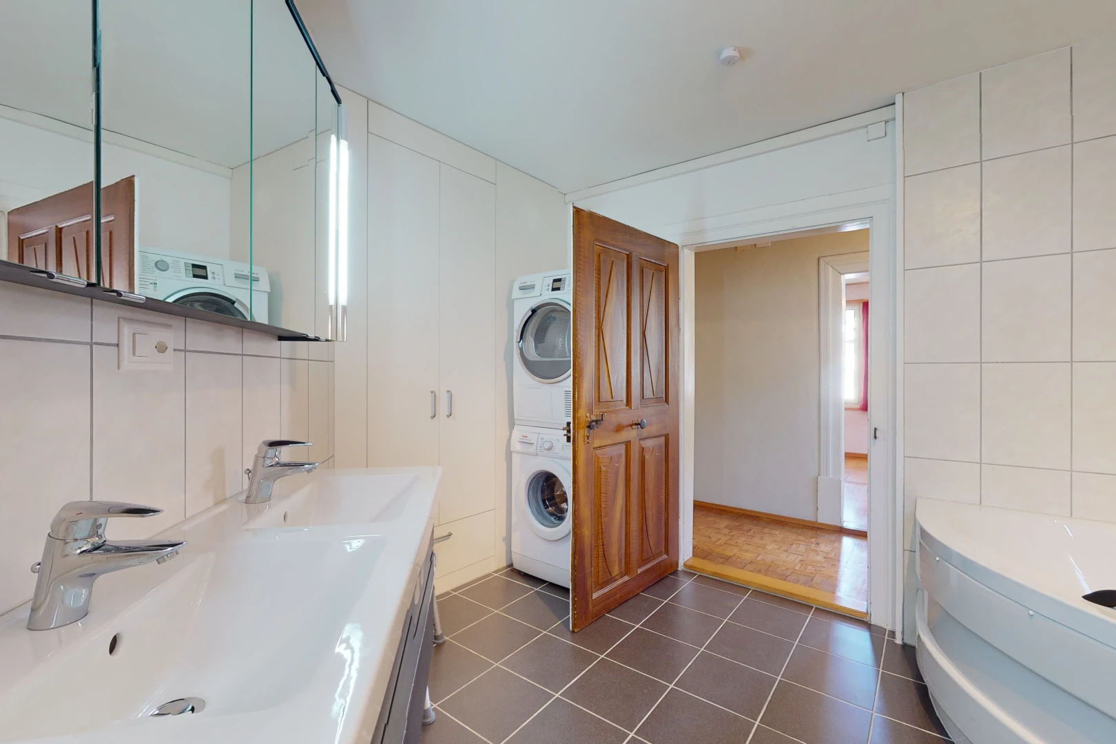 salle de bains avec carrelage, machine à laver / sèche-linge, meuble-lavabo, baignoire, double vasque, et miroir
