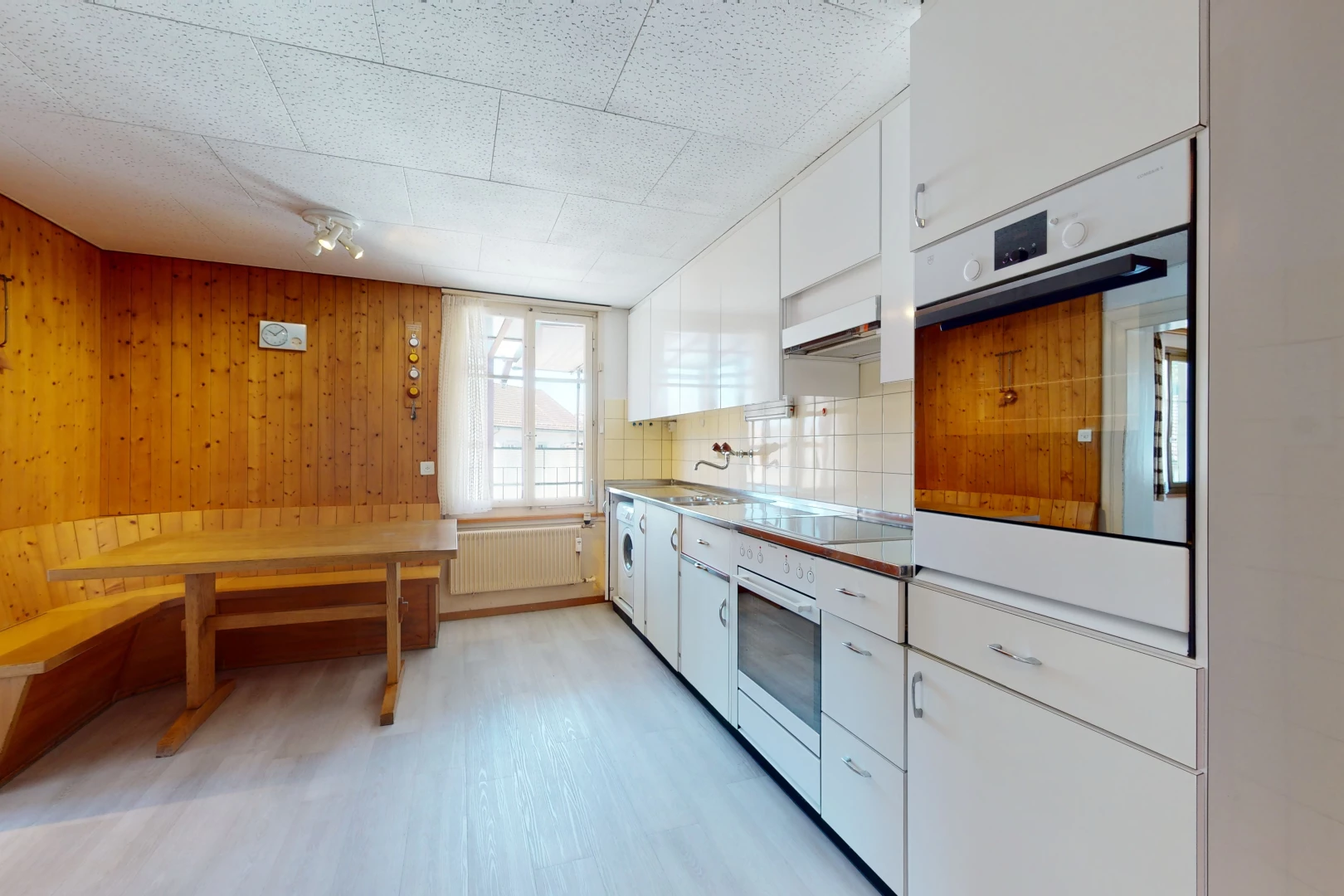 cuisine avec lumière naturelle, cuisinière électrique, four, radiateur, hotte, sol clair, et meubles marron