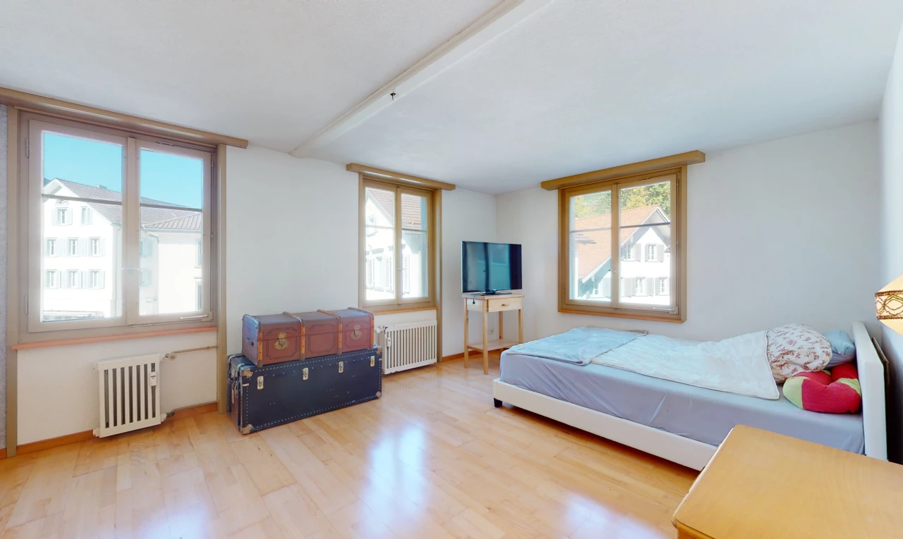 chambre à coucher avec lumière naturelle, poutres apparentes, parquet, radiateur, et télévision
