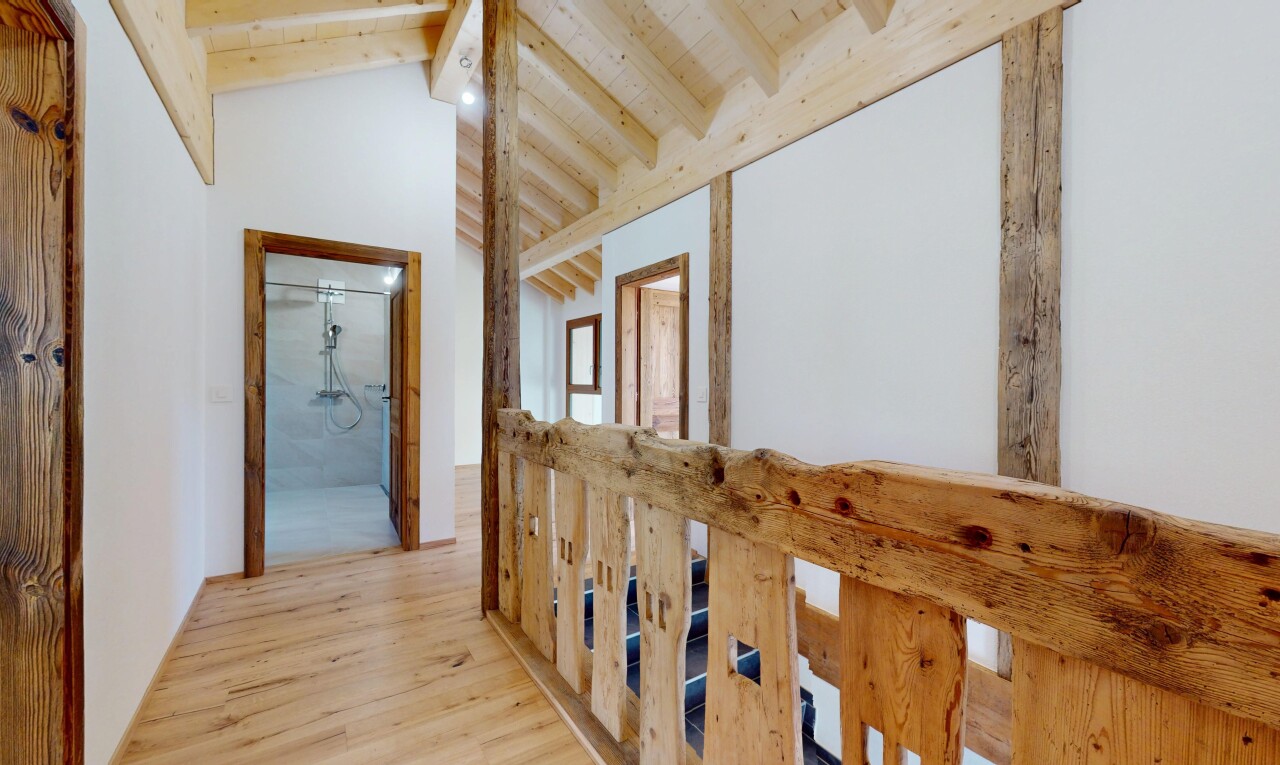 couloir avec cloison sèche, plafond voûté, sol en finition bois, plafond à poutres, et plafond haut
