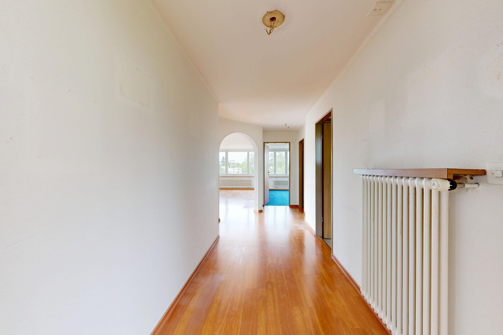 couloir avec cloison sèche, drywall, radiateur, sol en finition bois, et wood finish floor