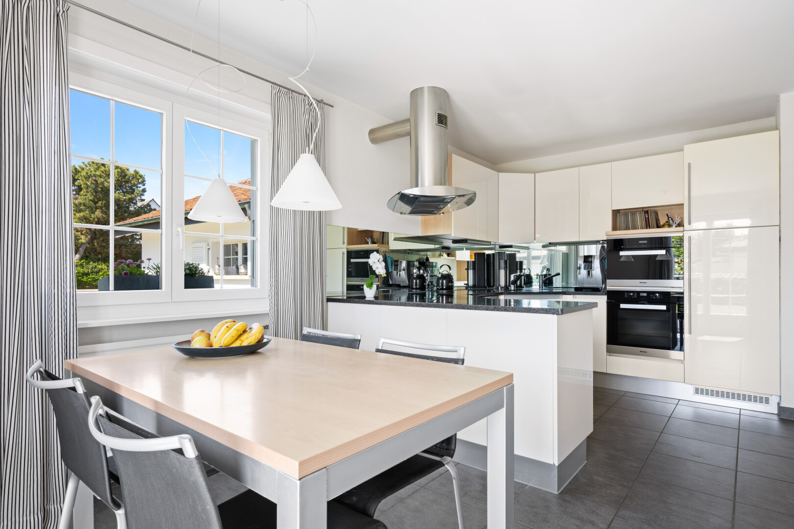 kitchen featuring dark countertops, range hood, a peninsula, white cabinetry, and a kitchen bar