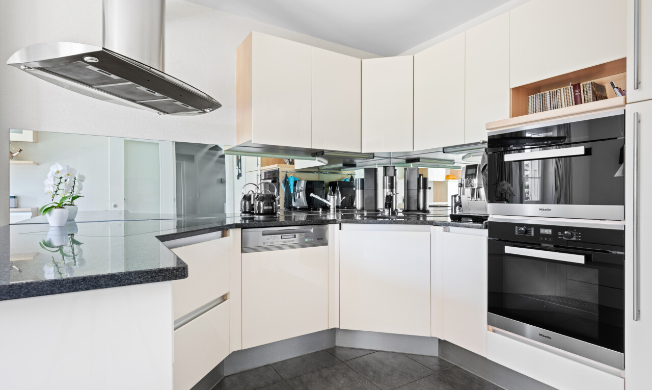 cuisine avec hotte, plans de travail en pierre, stone countertops, dark floor, et four double