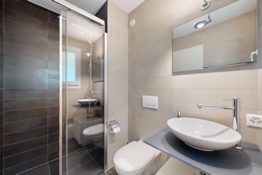 salle de bains avec vasque, toilettes, mur carrelé, miroir, et douche