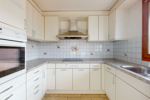 küche mit elektrischer herd, lüftungshaube, ofen, hellen fliesenböden, weissen schränken und hellen arbeitsplatten