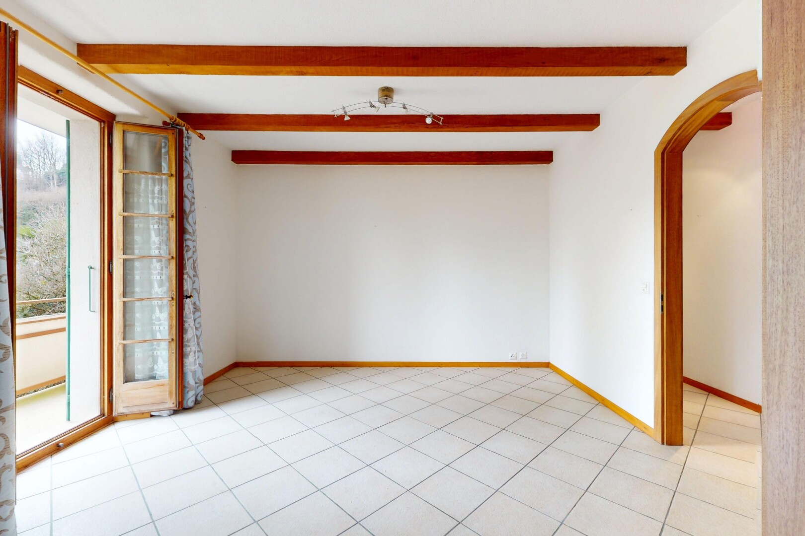 pièce vide avec lumière naturelle, cloison sèche, plafond à poutres, et passages en arc