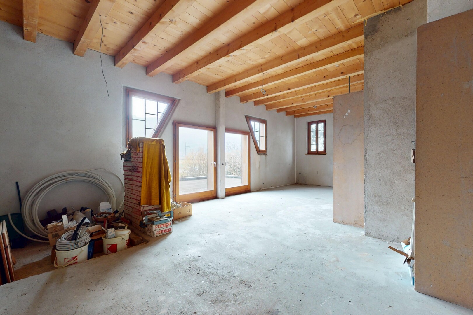 pièce vide avec mur en béton, lumière naturelle, et plafond à poutres