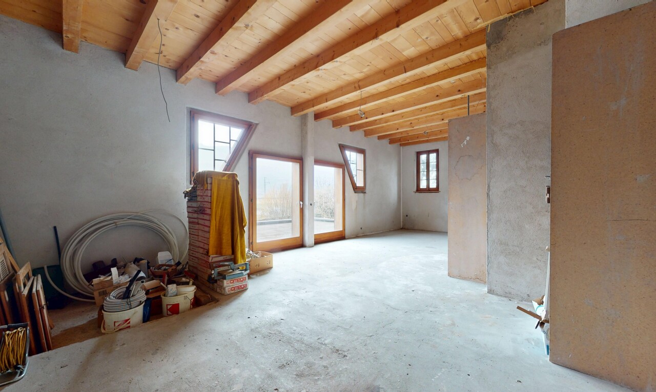pièce vide avec mur en béton, lumière naturelle, et plafond à poutres