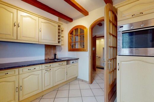 cuisine avec plafond à poutres, passages en arc, plans de travail, armoires crème, et four