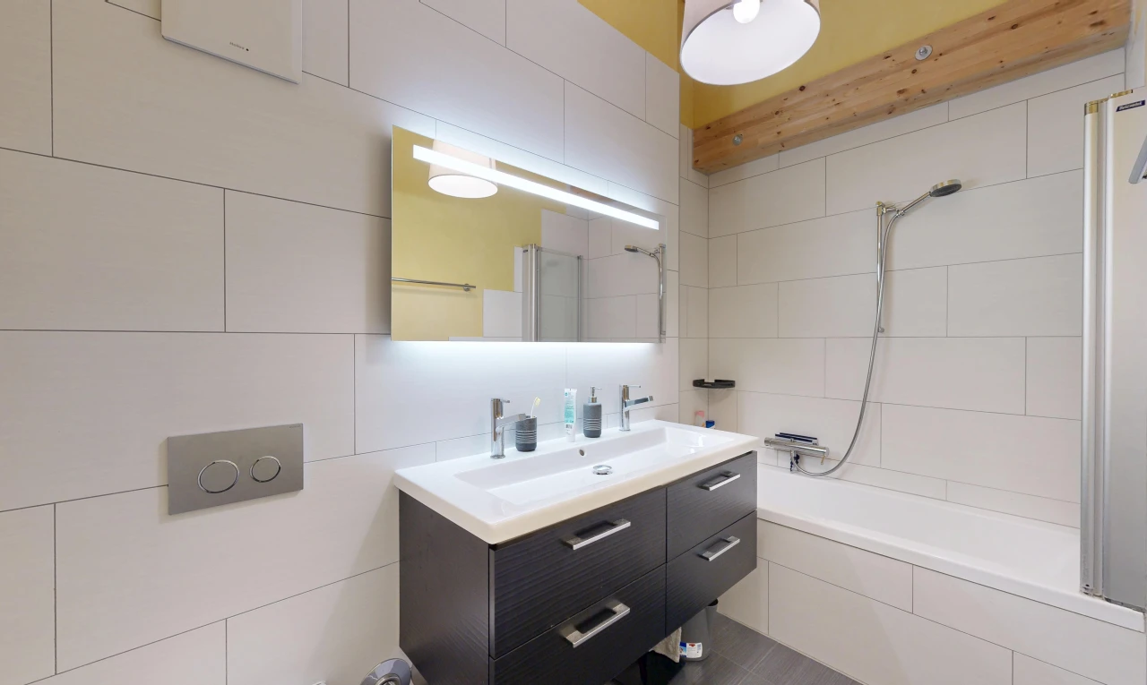salle de bains avec salle de bain complète, lavabo (ou coiffeuse selon le contexte), miroir, douche-bain combinés, et mur en carrelage