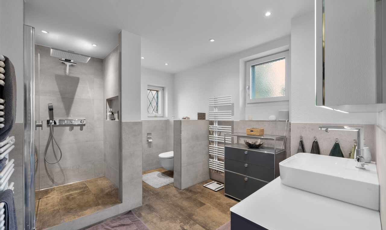 full bathroom featuring a towel warmer, tile walls, vanity, a wainscoted wall, and walk in shower