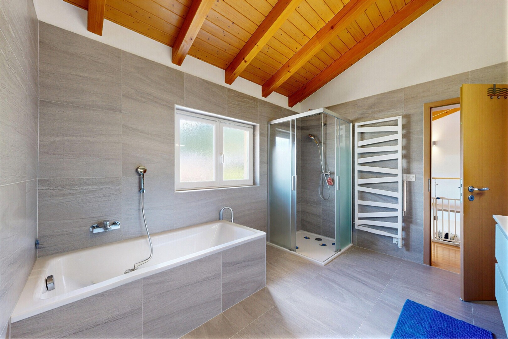 bathroom featuring double vanity, a stall shower, a towel warming rack, tile walls, and vaulted ceiling with beams
