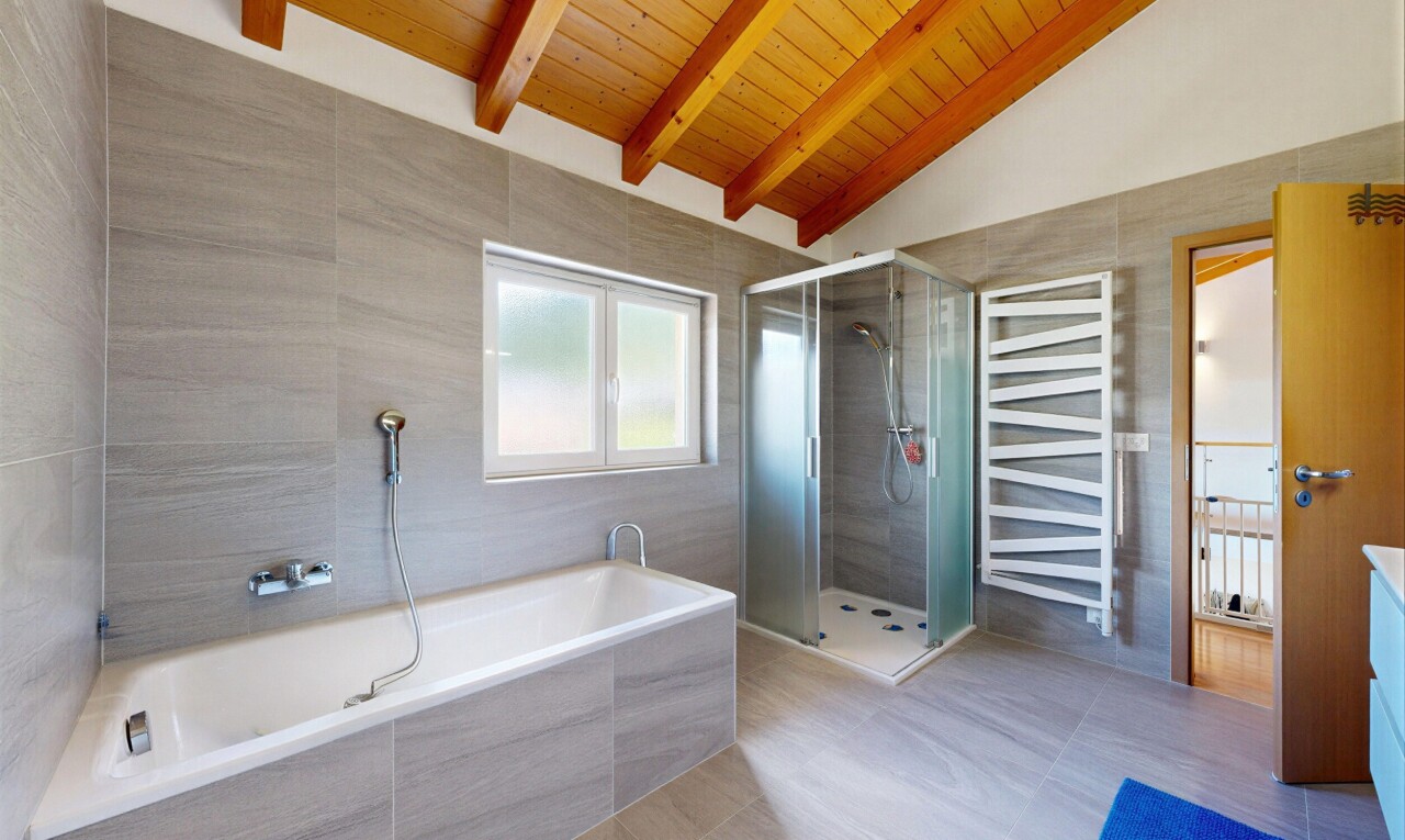bathroom featuring double vanity, a stall shower, a towel warming rack, tile walls, and vaulted ceiling with beams