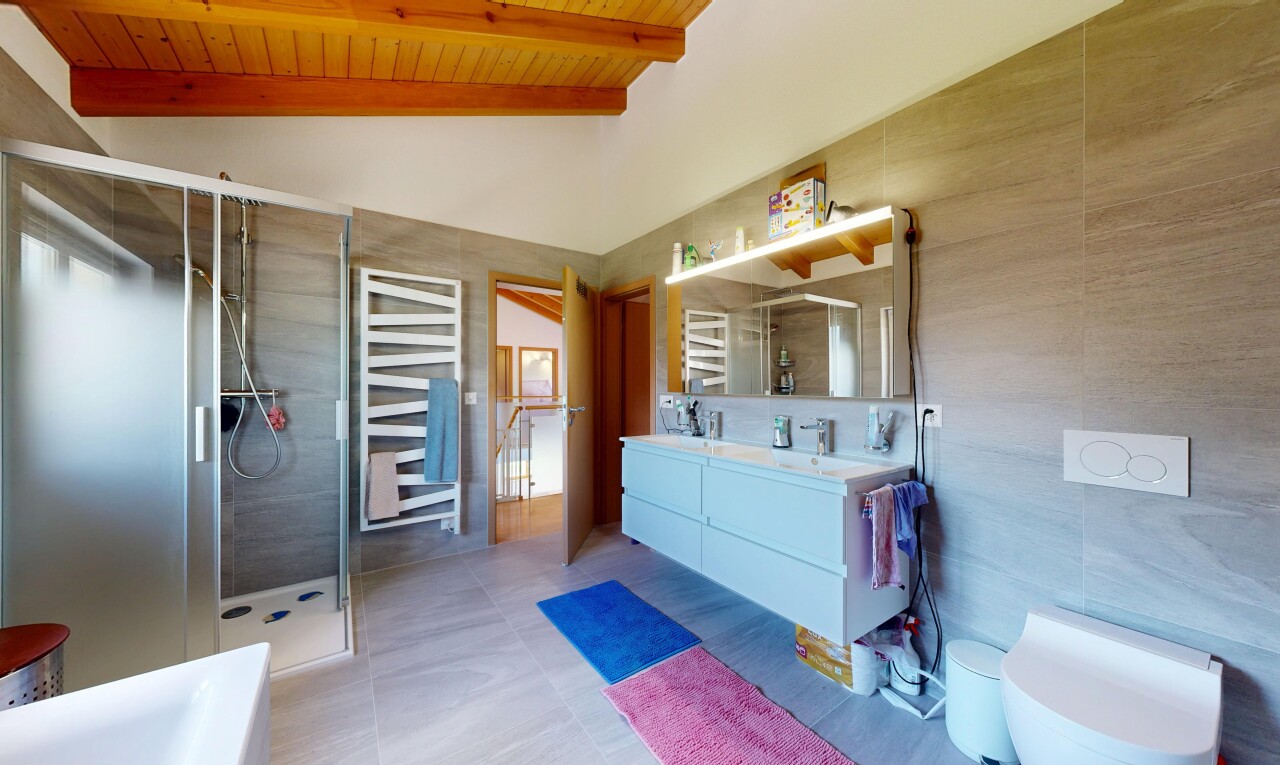 bathroom featuring double vanity, a stall shower, a towel warming rack, tile walls, and vaulted ceiling with beams