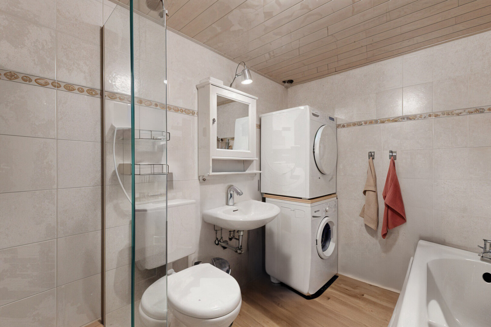 salle de bains avec vasque, miroir, machine à laver / sèche-linge superposés, plancher de bois, et mur carrelé