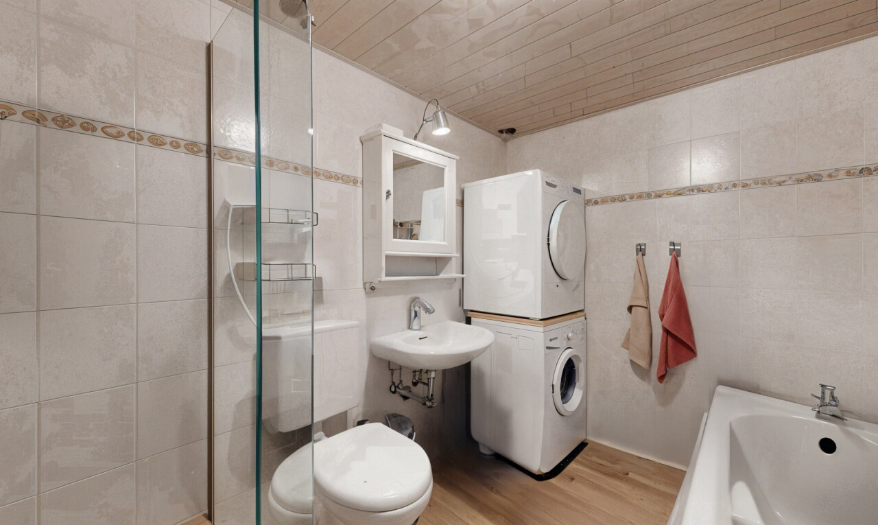 salle de bains avec vasque, miroir, machine à laver / sèche-linge superposés, plancher de bois, et mur carrelé